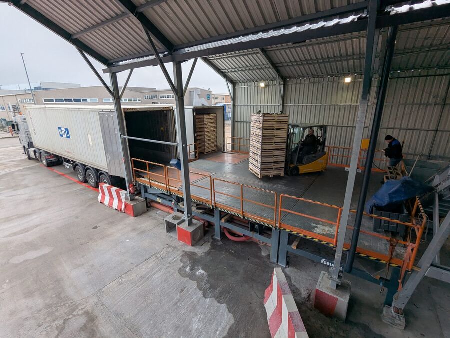 Prevzem: tovornjak s paletami na nakladalni rampi hale, viličar razklada palete.
